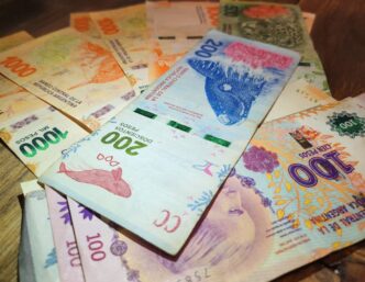 Notas de peso argentino em contagem, indicando a desvalorização da moeda e o acordo de swap entre EUA e Argentina.