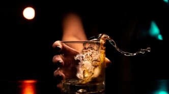 Homem bebe em um copo com gelo em um bar, refletindo o tema do medo de beber após adulteração por metanol.