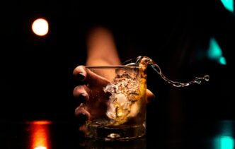 Homem bebe em um copo com gelo em um bar, refletindo o tema do medo de beber após adulteração por metanol.
