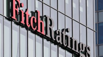 Logotipo da agência Fitch Ratings sobre gráfico de indicadores econômicos dos EUA.